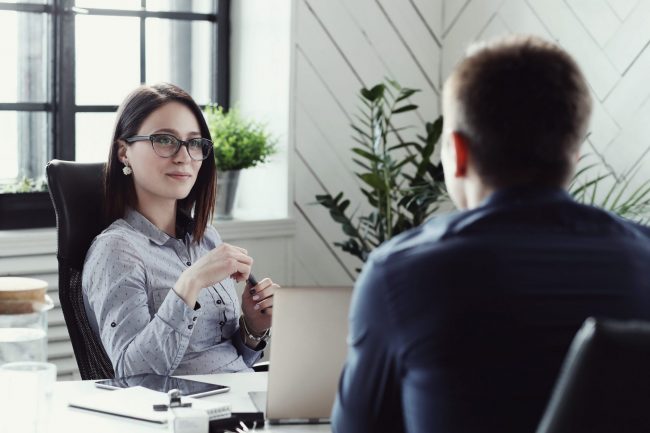 Photo of female executive sitting behind desk looking at man illustrates blog "What is EPLI and Who Needs It?"