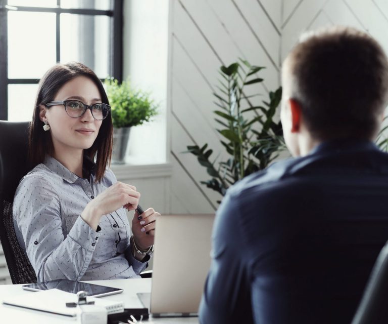 Photo of female executive sitting behind desk looking at man illustrates blog "What is EPLI and Who Needs It?"