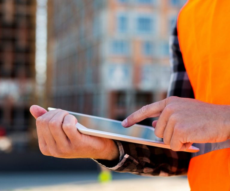 Closeup of man in safety vest holding tablet illustrates blog "The Pandemic and the Rising Costs of Building"