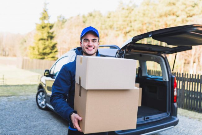 Man carrying boxes in front of delivery van illustrates blog "Is Commercial Auto Insurance Required in California?"