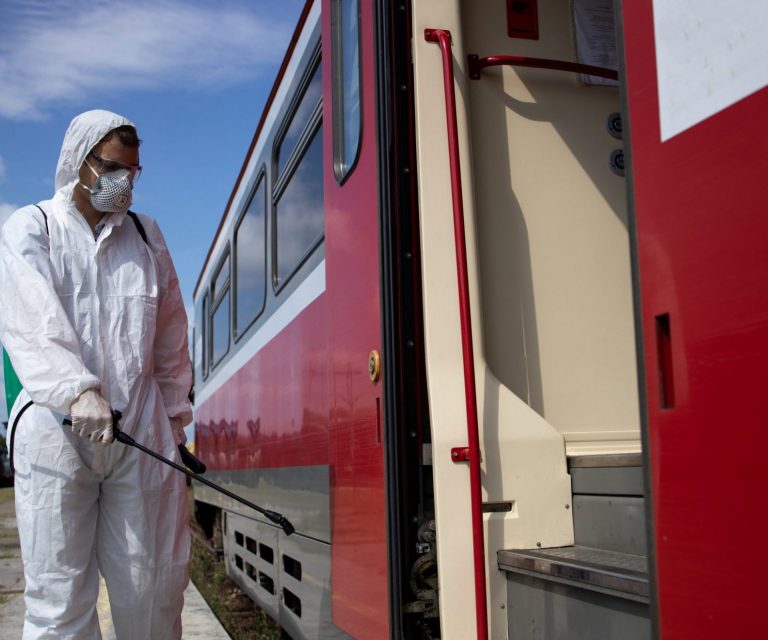 Man in white protection suit disinfecting and sanitizing subway train exterior to stop spreading highly contagious corona virus. Man in hazmat suit by truck illustrates blog "What Is Hazmat Truck Insurance?"