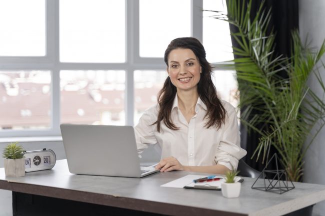 Woman sitting in office in front of laptop illustrates blog "Professional Liability Insurance vs General Liability: What Is the Difference?"